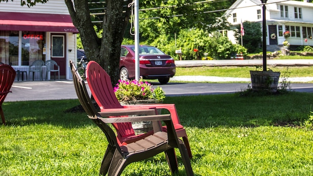 A flagpole with an American flag, a red Adirondack chair, and a building with a red awning in the background. - Fran Cove Motel (Lake George)