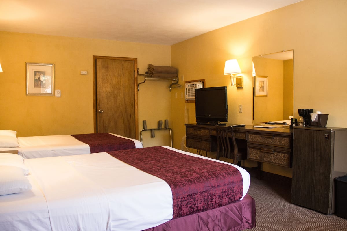 Une chambre d’hôtel avec deux lits, un bureau avec un ordinateur, une télévision et un miroir.