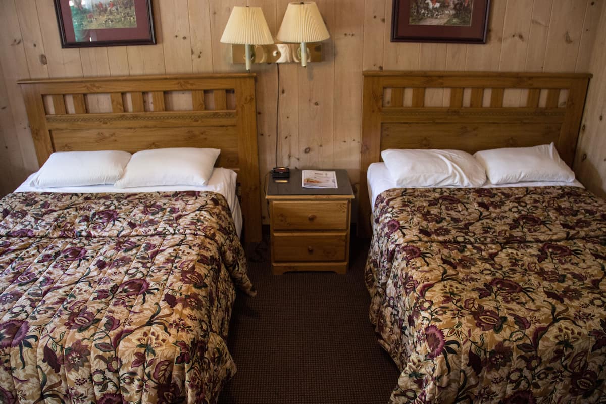 Une chambre avec deux lits en bois, chacun agrémenté d’une literie à motifs floraux. On y trouve deux tables de chevet avec des lampes et un petit tiroir.