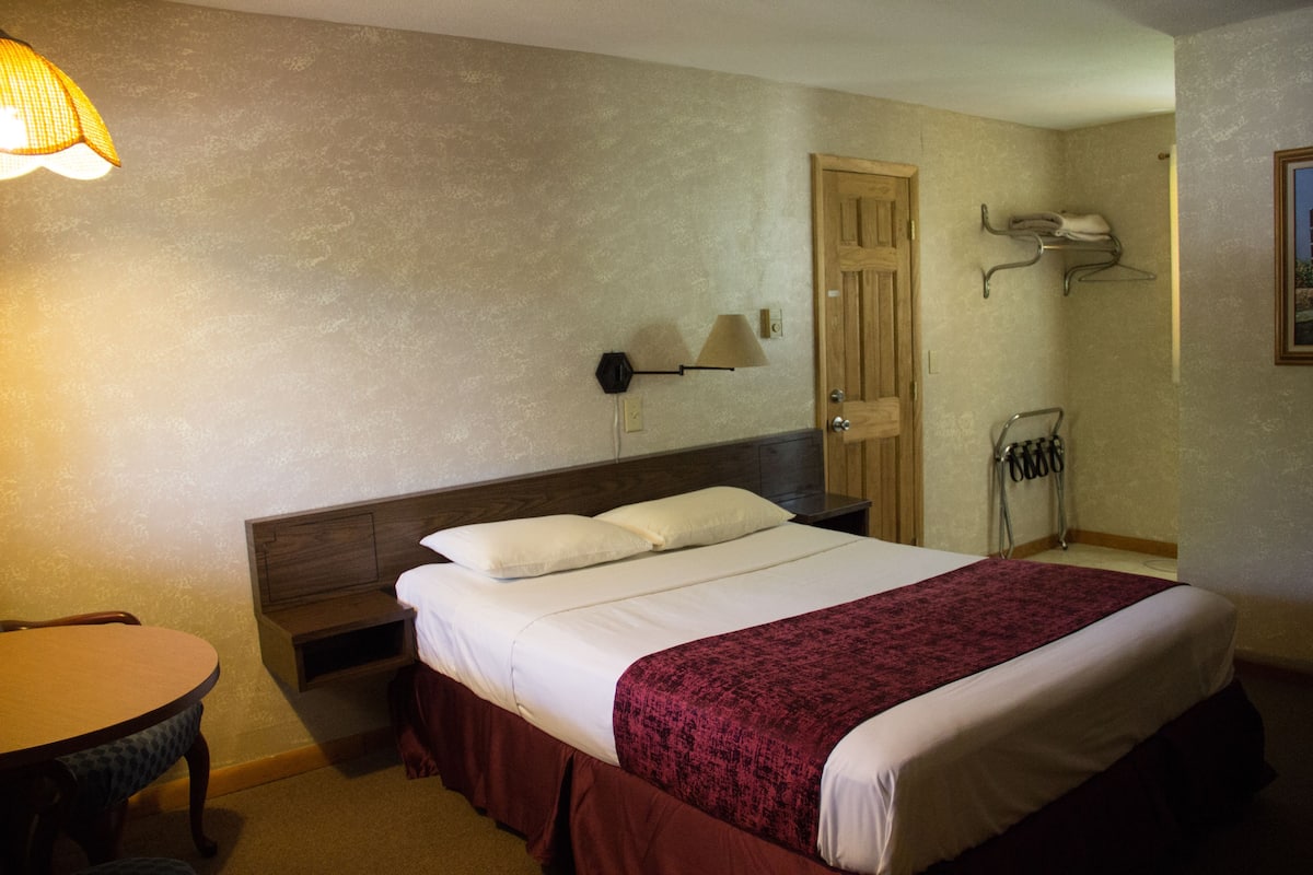 Une chambre d’hôtel avec un lit, une table de chevet, une lampe, une chaise et une porte.