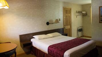 A hotel room with a bed, a nightstand, a lamp, a chair, and a door.
