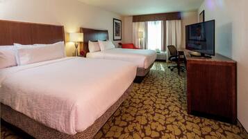 A hotel room with two beds, a desk with a television, a chair, and a lamp.