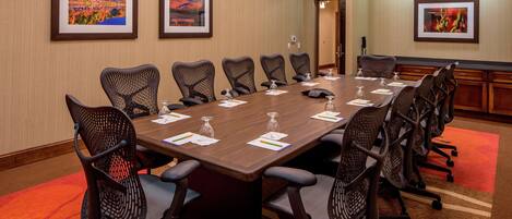 A conference room with a long table, multiple chairs, and framed pictures on the walls.
