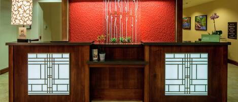 A reception desk with a wooden finish, a red textured wall behind it, and a hanging light fixture.