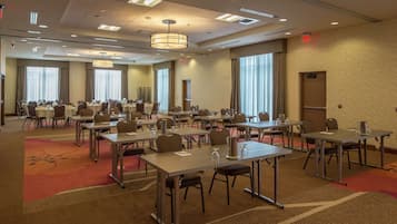 A conference room with multiple tables and chairs, large windows, and a carpeted floor.