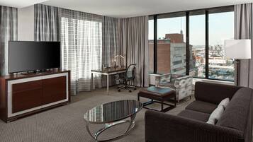 A modern hotel room with a large TV, a desk, a comfortable sofa, and a glass coffee table.