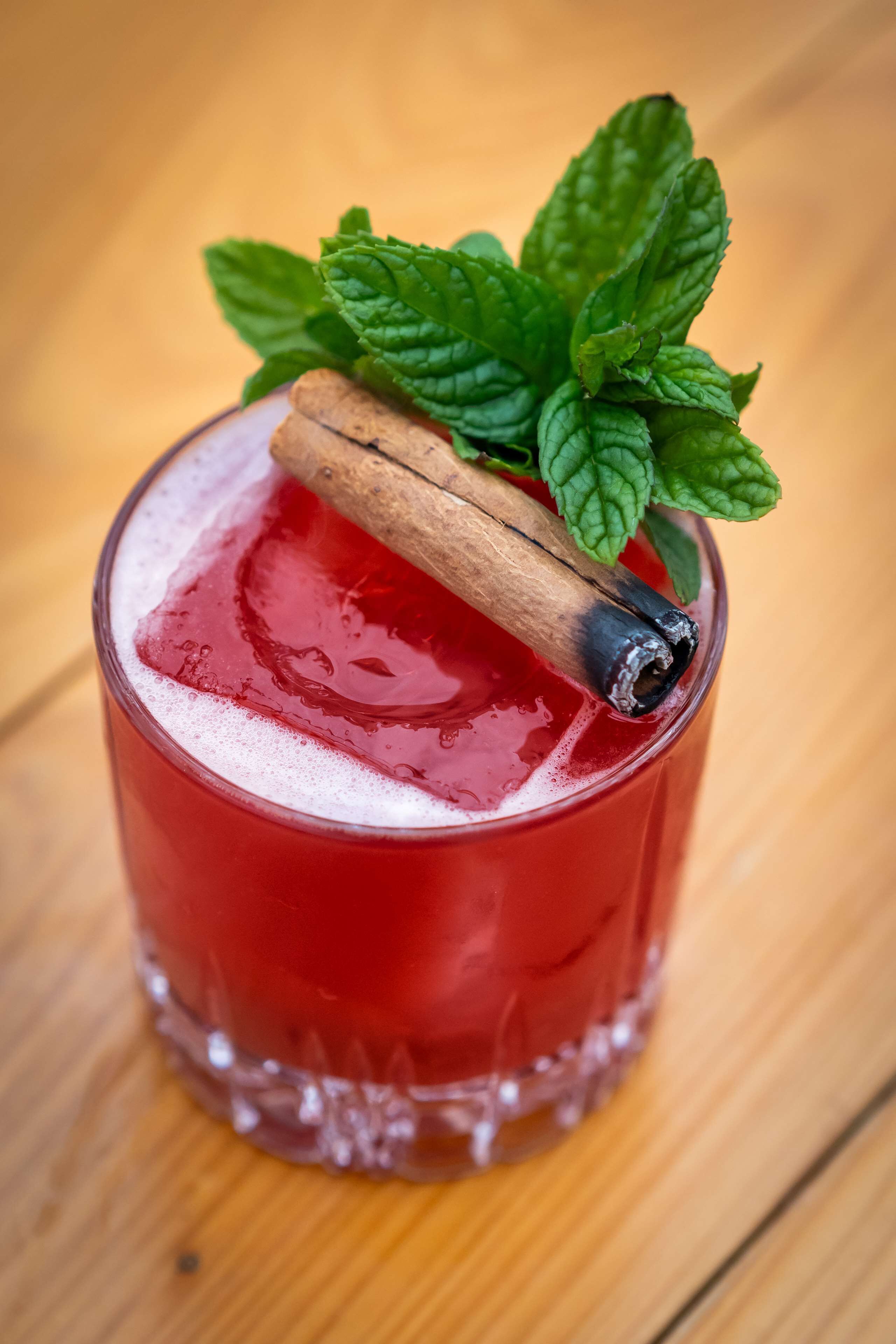 Un verre contenant une boisson rouge, une tige de cannelle et des feuilles de menthe.