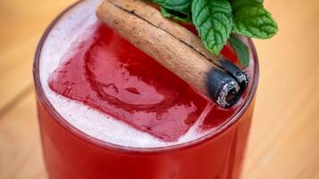 A glass with a red beverage, a cinnamon stick, and mint leaves.