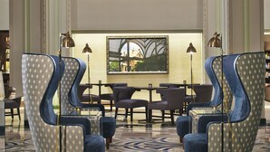 A spacious lobby with high ceilings, large windows, and a modern chandelier. There are several seating areas with blue upholstered chairs and a patterned rug on the floor. - Hilton Garden Inn Phoenix Downtown (Phoenix)