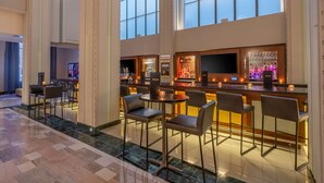 A spacious bar area with high ceilings and large windows, featuring a bar counter, seating, and a television screen. - Hilton Garden Inn Phoenix Downtown (Phoenix)