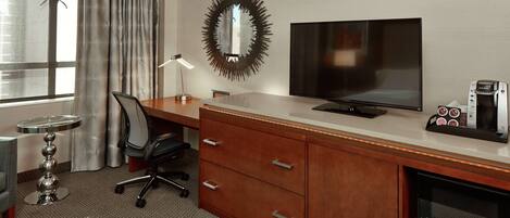 A hotel room with a wooden desk, a flat-screen TV, a coffee maker, and a microwave.