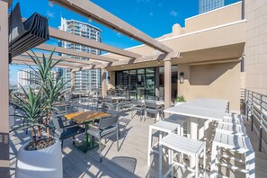 An outdoor patio area with tables and chairs, a potted plant, and a view of high-rise buildings. - Hilton Garden Inn Phoenix Downtown (Phoenix)