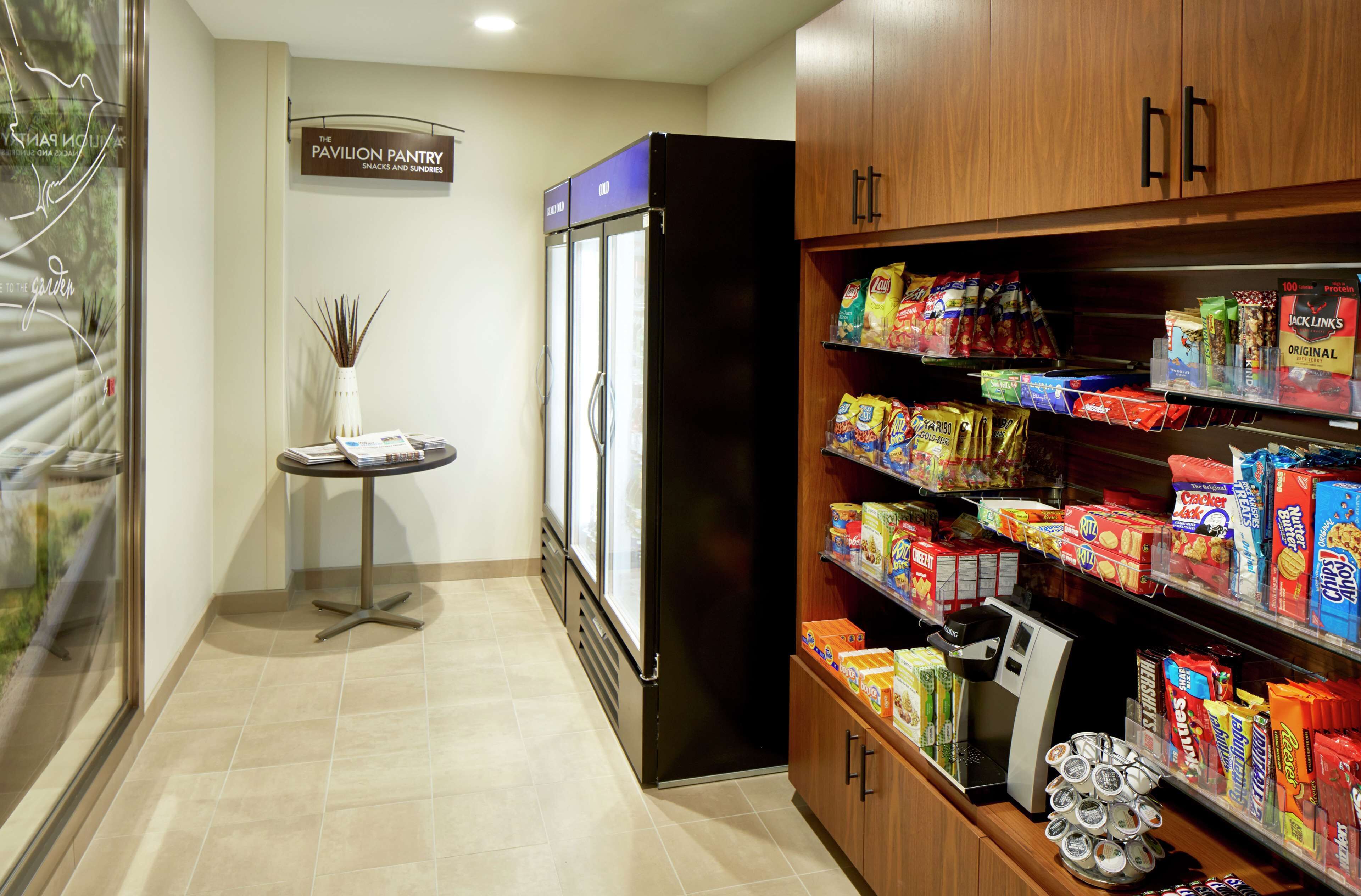 A kitchenette area with a refrigerator, pantry shelves stocked with snacks, and a coffee machine.