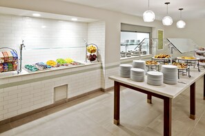 A buffet setup with various food items and stacked plates. - Hilton Garden Inn Phoenix Downtown (Phoenix)