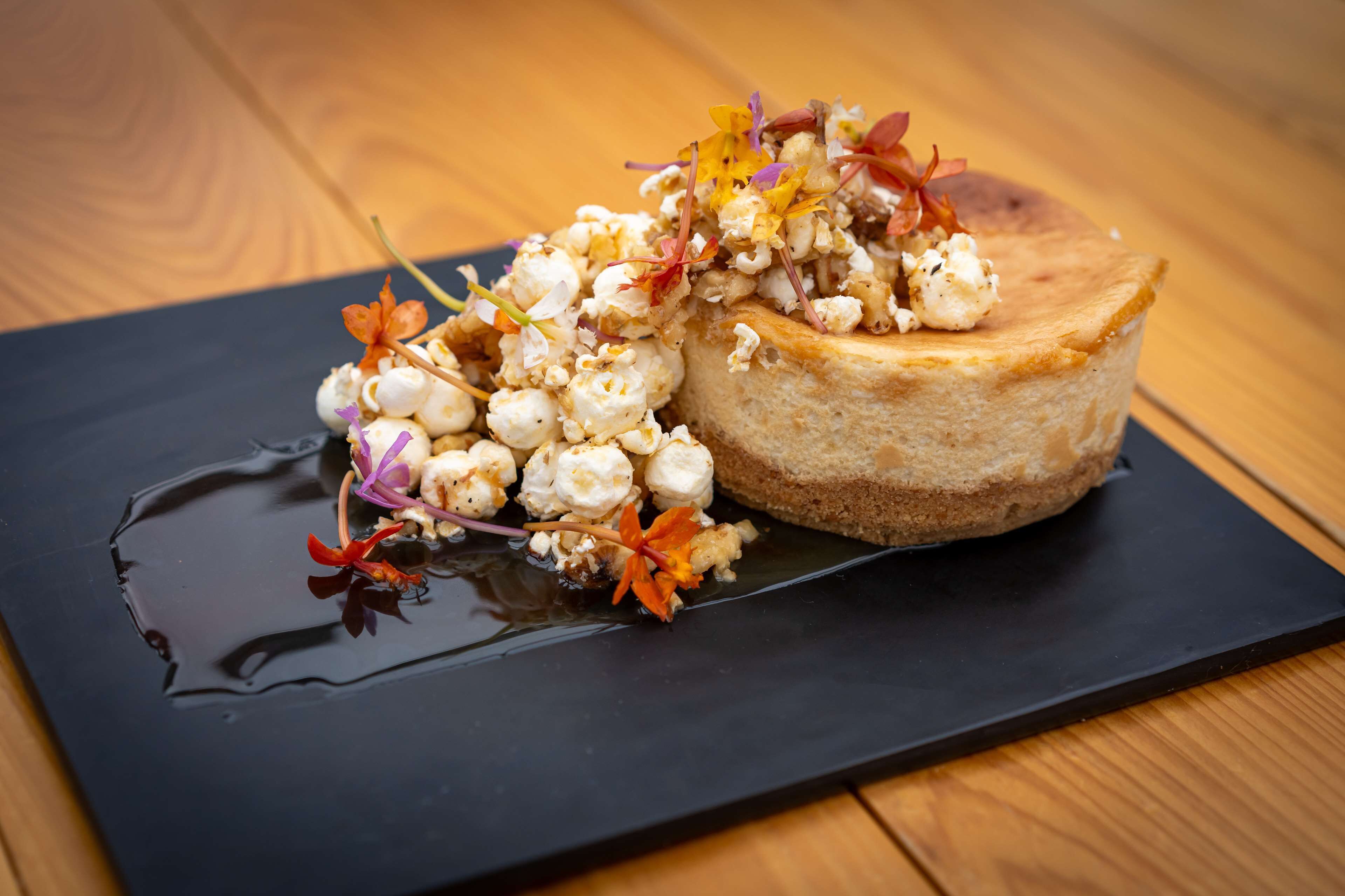 Un postre sobre un plato negro, con una mesa de madera de fondo.