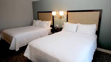 Habitación de hotel con dos camas individuales, una mesita de noche con lámpara y un aplique de pared.