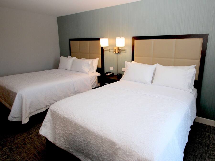 Habitación de hotel con dos camas individuales, una mesita de noche con lámpara y un aplique de pared.