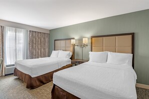Habitación de hotel con dos camas, una mesita de noche, una lámpara y una ventana con cortinas.
