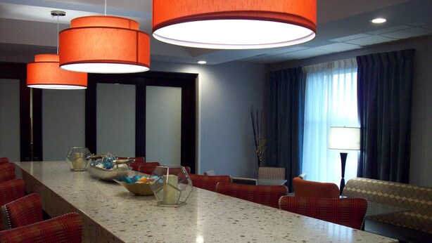 A conference room with a long table, red upholstered chairs, and orange pendant lights. - Hampton Inn Suffolk (Suffolk)
