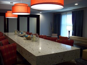 A conference room with a long table, red upholstered chairs, and orange pendant lights.