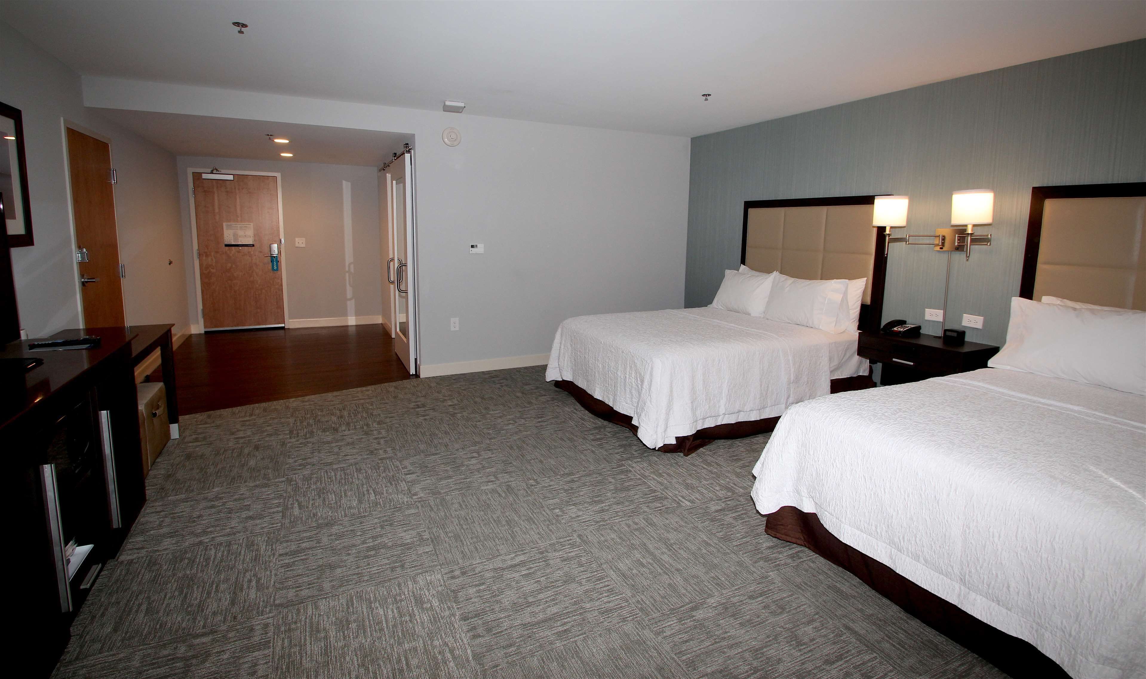 A hotel room with two beds, a desk, a chair, a dresser, and a bathroom door.
