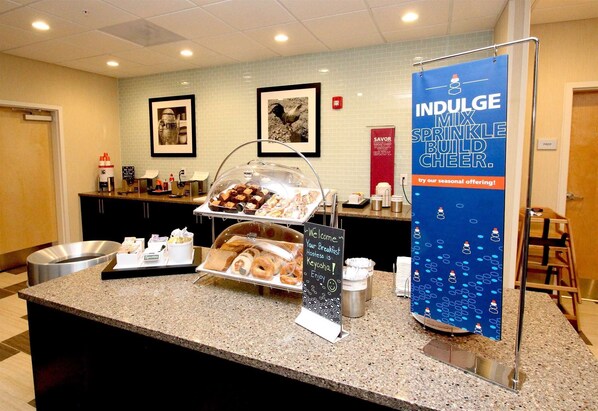 A breakfast buffet counter with various food items and a promotional banner.
