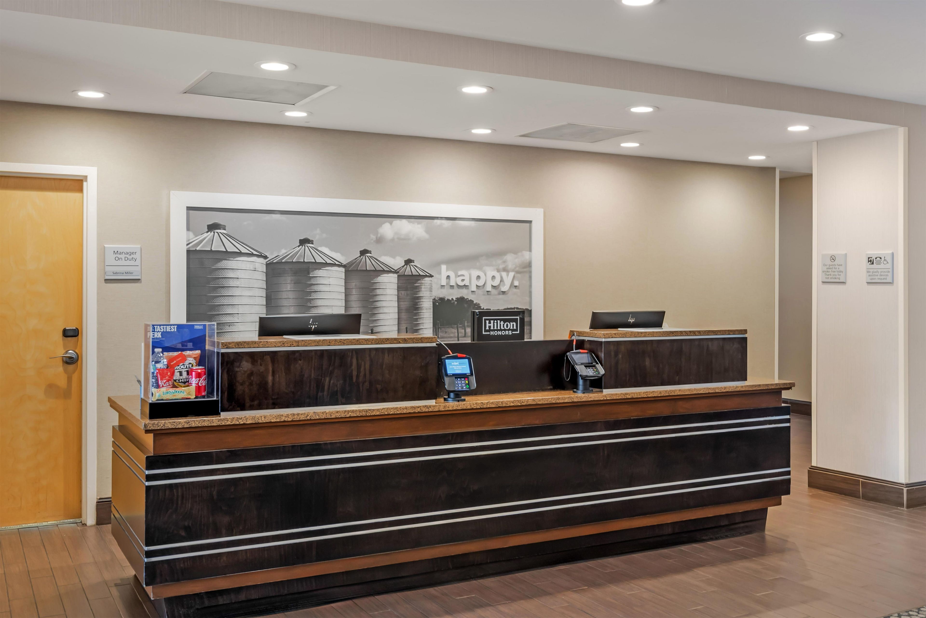 A hotel reception desk with a large framed picture above it, a digital screen, and a minibar.