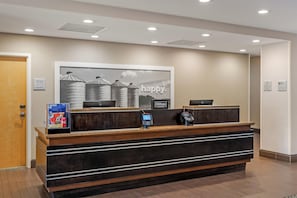 Un mostrador de recepción de hotel con una gran foto enmarcada encima, una pantalla digital y una minibar.
