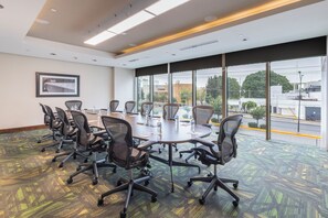 A conference room with a large table, multiple chairs, and large windows offering a view of the street. - Hampton Inn by Hilton Leon Guanajuato (León)