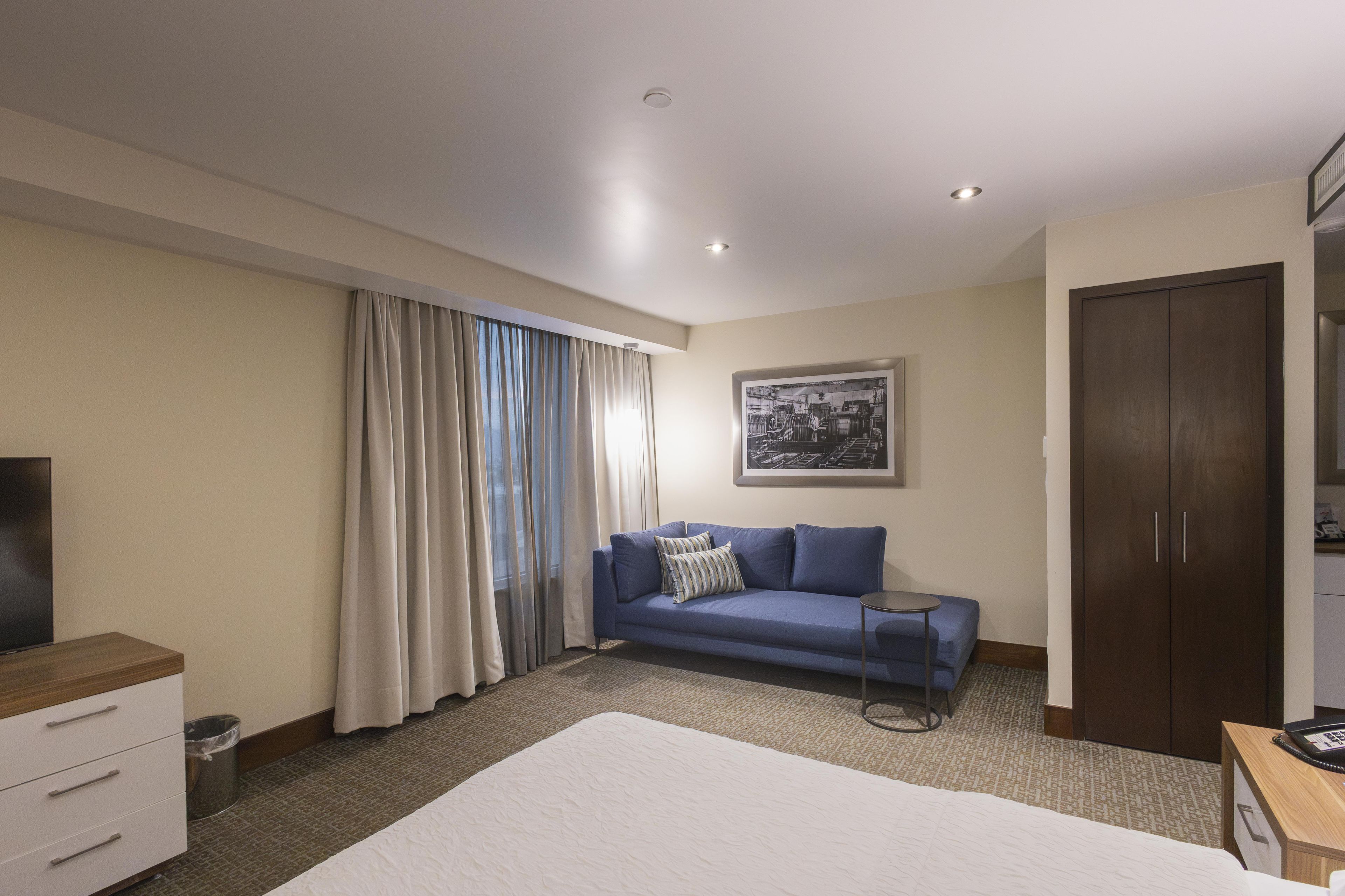 Una habitación de hotel con una cama, un sofá azul, un armario de madera, un televisor y un cuadro en la pared.