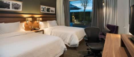 Une chambre d’hôtel avec deux lits, un bureau, une chaise et une grande fenêtre avec des rideaux.