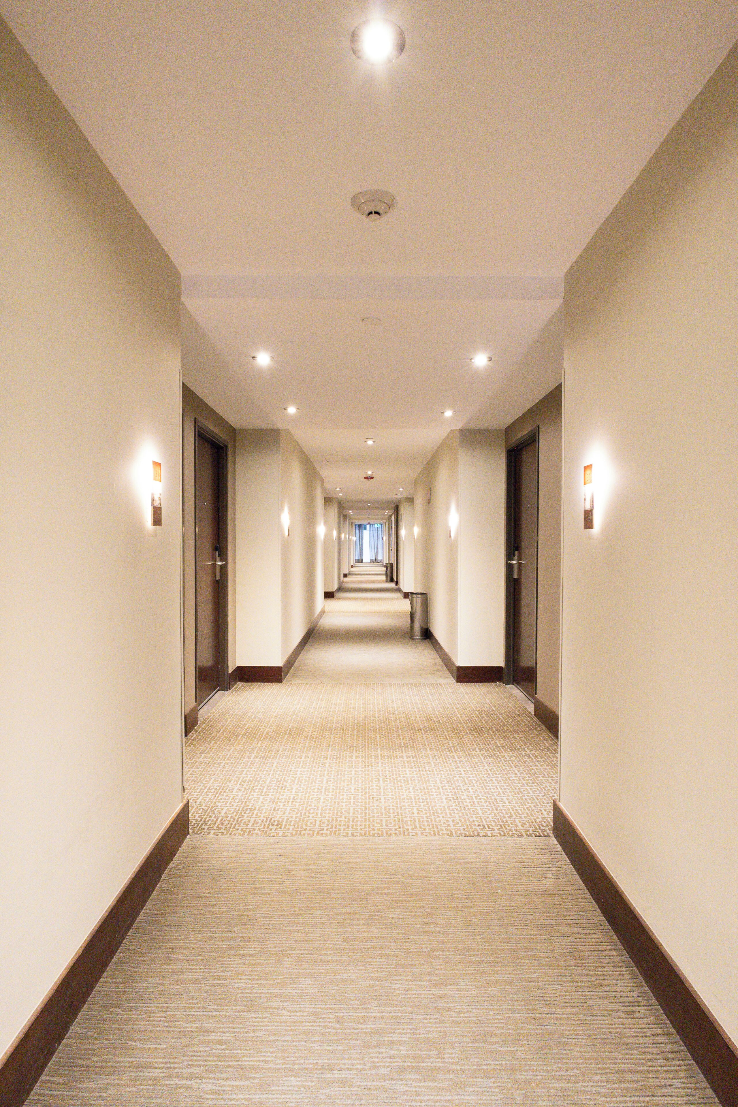A hotel hallway with carpeted floors, doors on both sides, and recessed lighting.