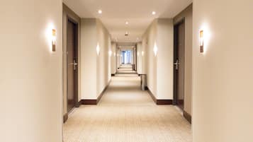 A hotel hallway with carpeted floors, doors on both sides, and recessed lighting.