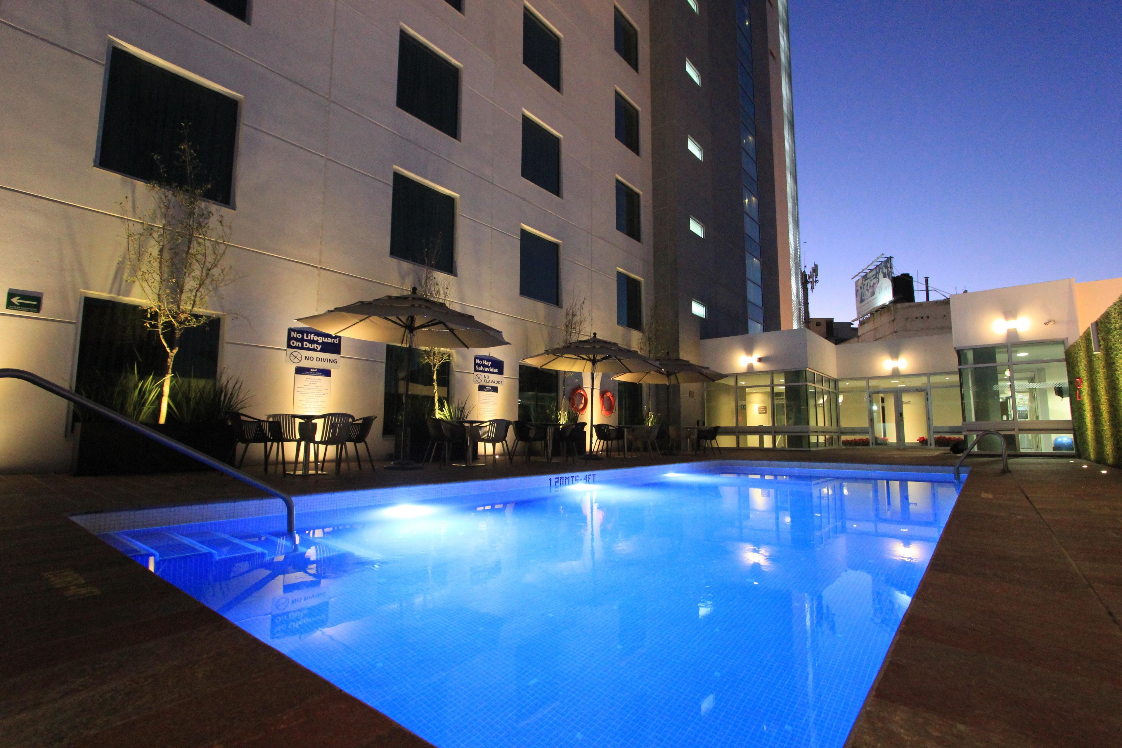 Una piscina exterior con solárium alicatado, rodeada de mobiliario y sombrillas.