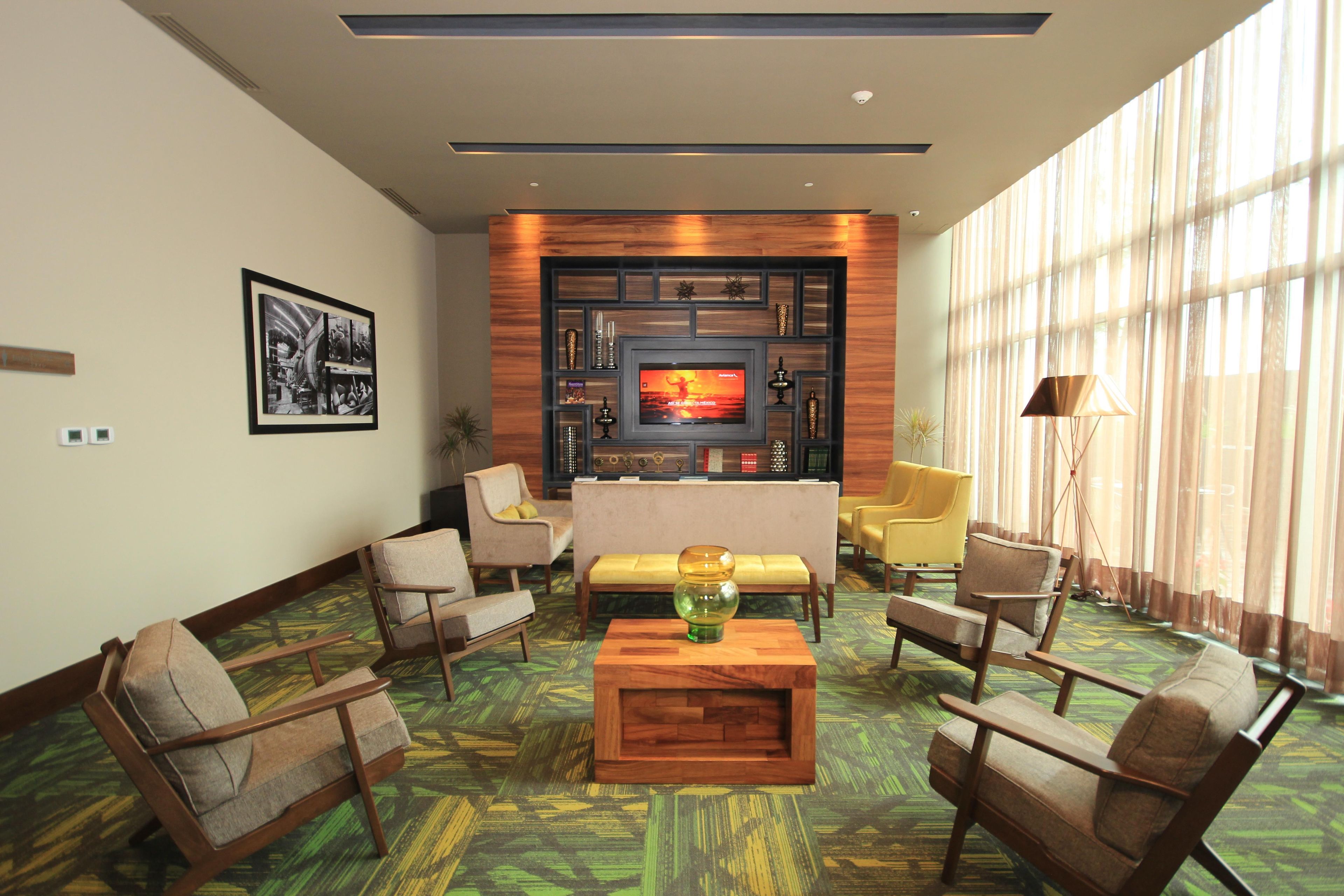 A hotel lobby with a central seating area, a television, and a large window with curtains.