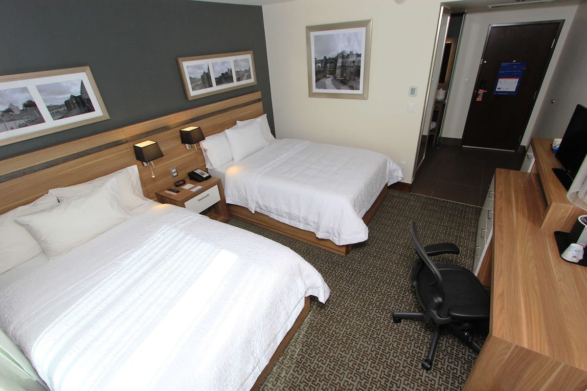 Una habitación de hotel con dos camas, un escritorio, una silla y un televisor.