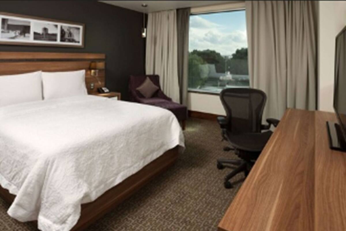 Habitación de hotel con una cama grande, un escritorio, una silla y una ventana con vista a un cuerpo de agua.