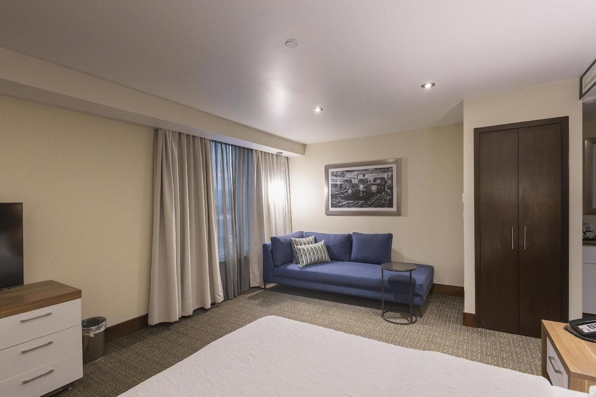 Habitación de hotel con cama, sofá azul, armario, mesita y televisor.