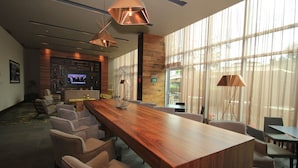 Un moderno vestíbulo de hotel con mostrador de recepción de madera, asientos cómodos, televisión y ventanas amplias.