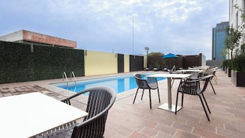 Zona de piscina en la azotea con una piscina azul cristalina, rodeada de mobiliario exterior y un seto verde.