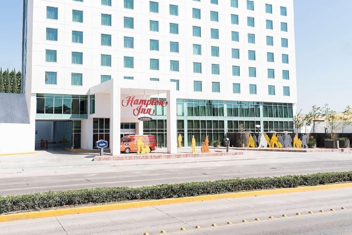 Un hotel moderno con un llamativo letrero de Hampton Inn, ventanas amplias y una fachada plana.