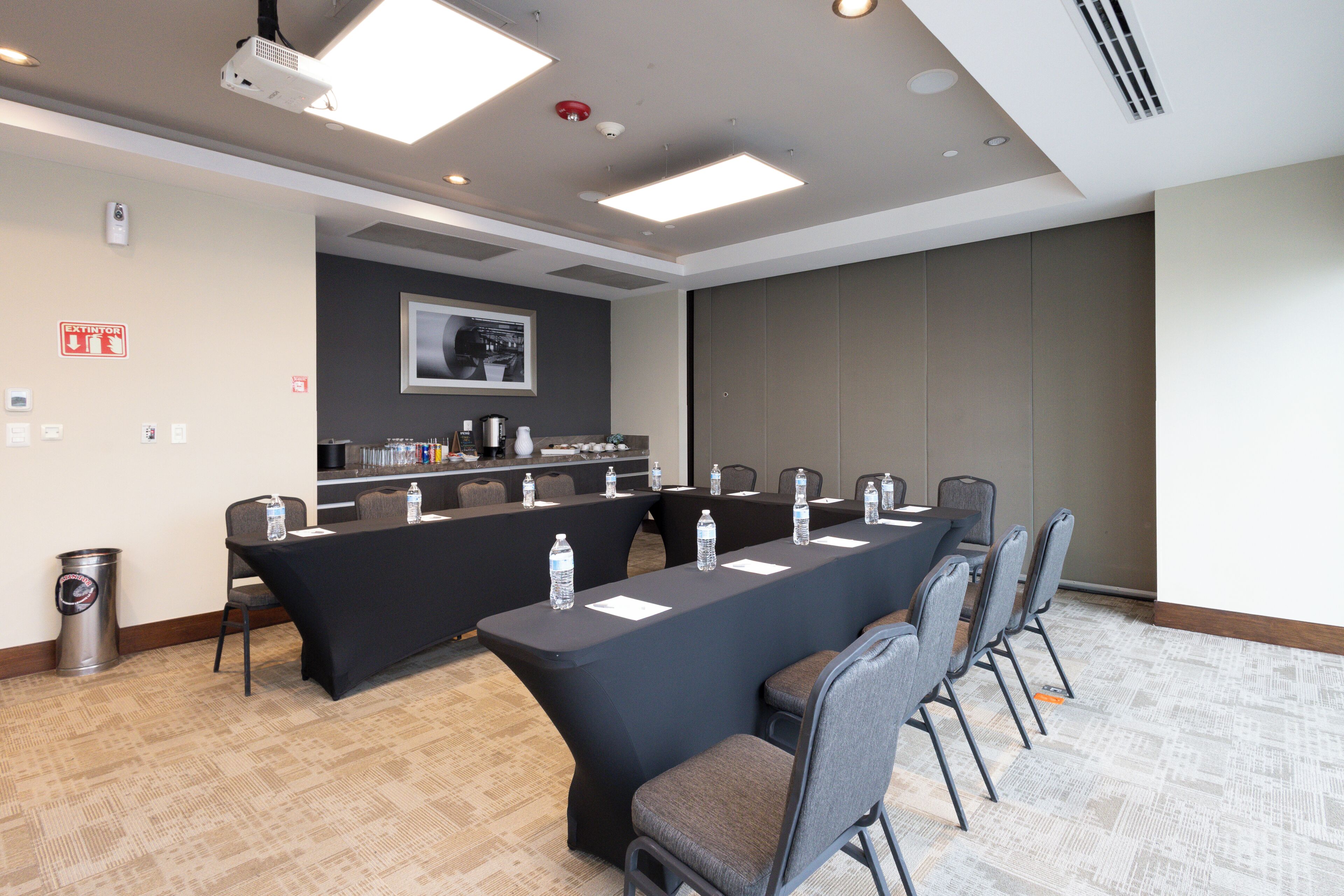 A conference room with a long table, chairs, water bottles, a projector, and a fire extinguisher.