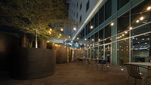 Un patio al aire libre con mesas y sillas, una maceta grande y luces colgantes.