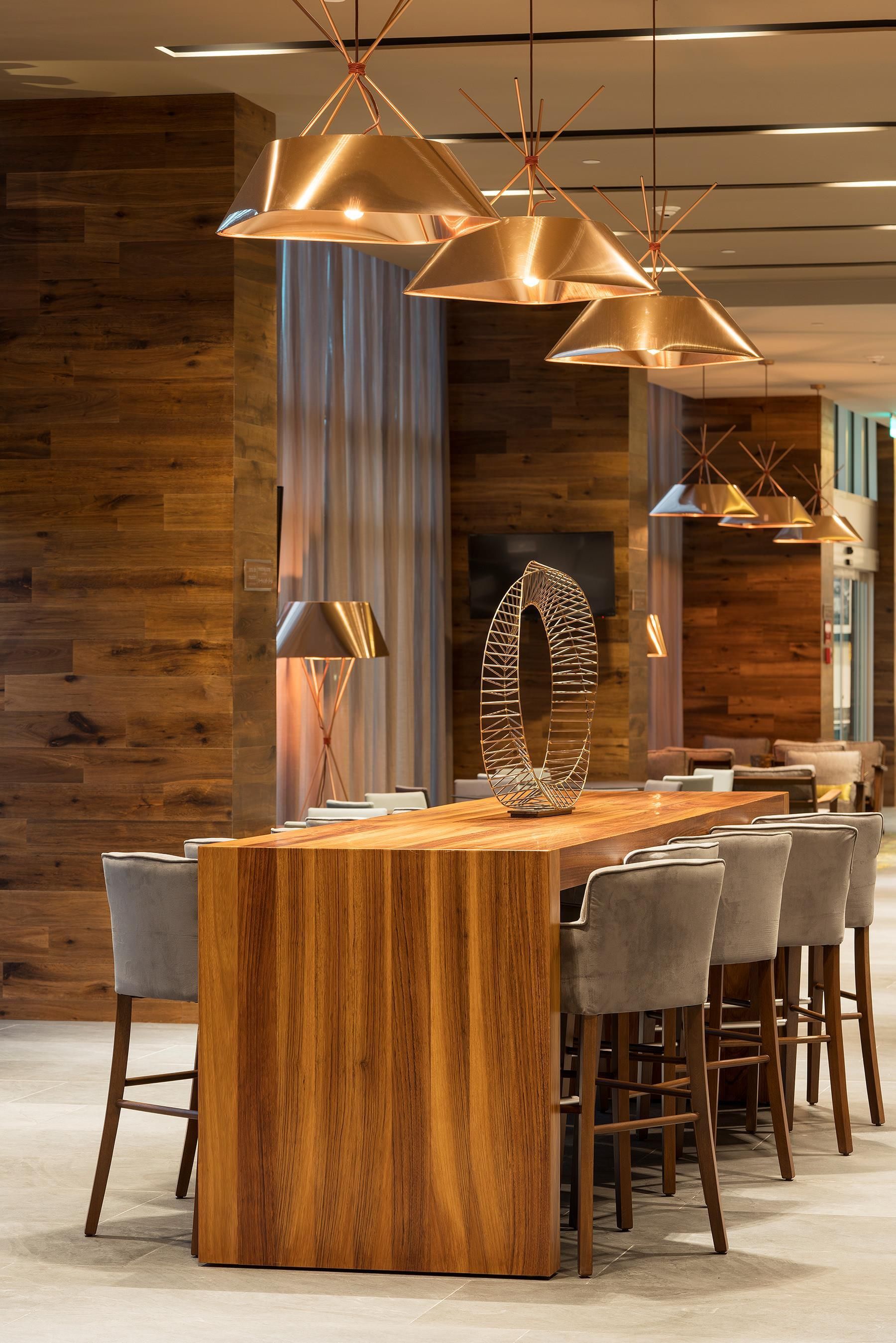 A modern dining area with a wooden bar, grey upholstered chairs, and pendant lighting.
