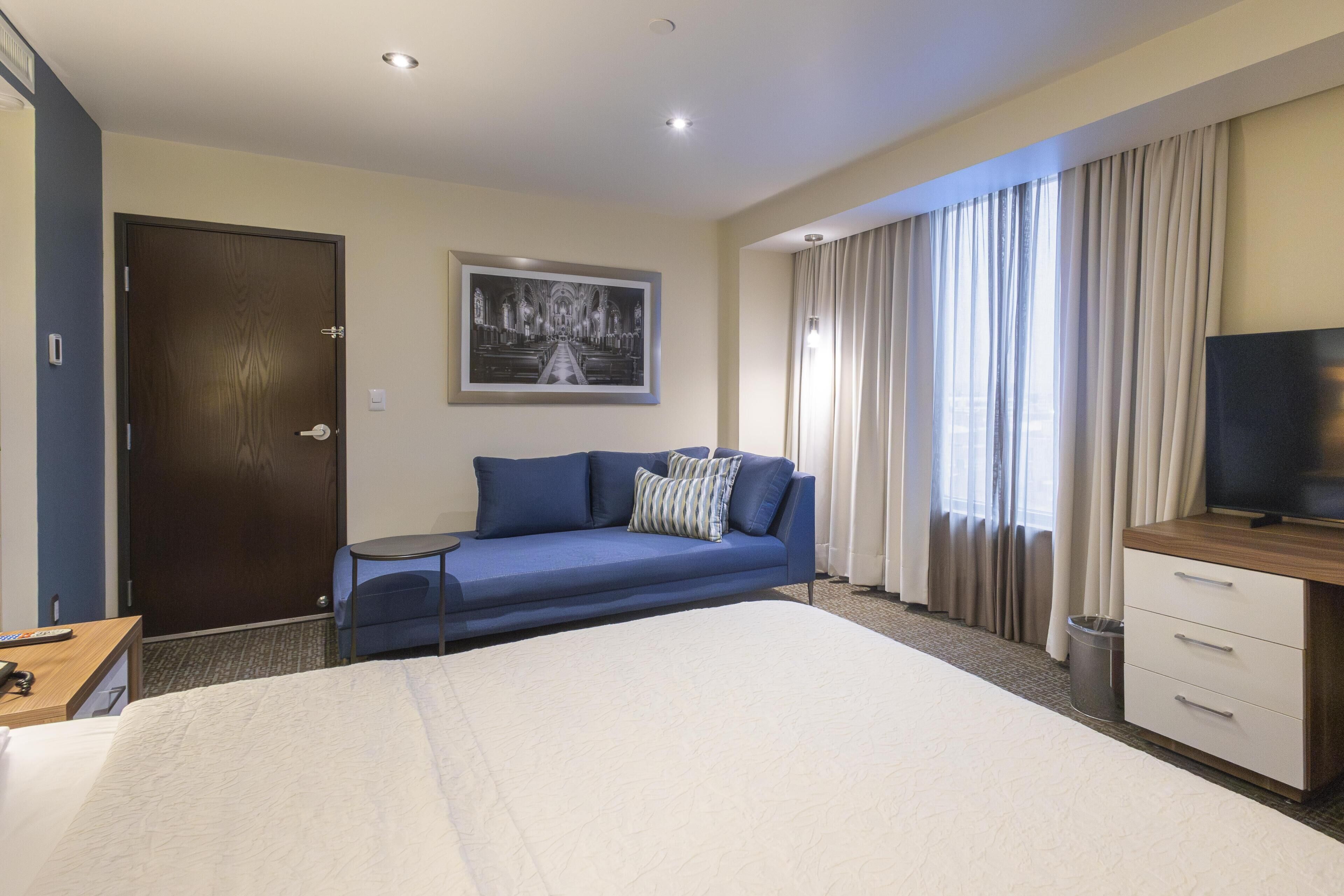 Una habitación de hotel con una cama, un sofá, un televisor, un escritorio y un cuadro en la pared.