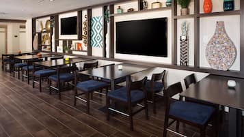 Een moderne eetruimte met meerdere tafels en stoelen, een grote flatscreen televisie en decoratieve wandplanken.