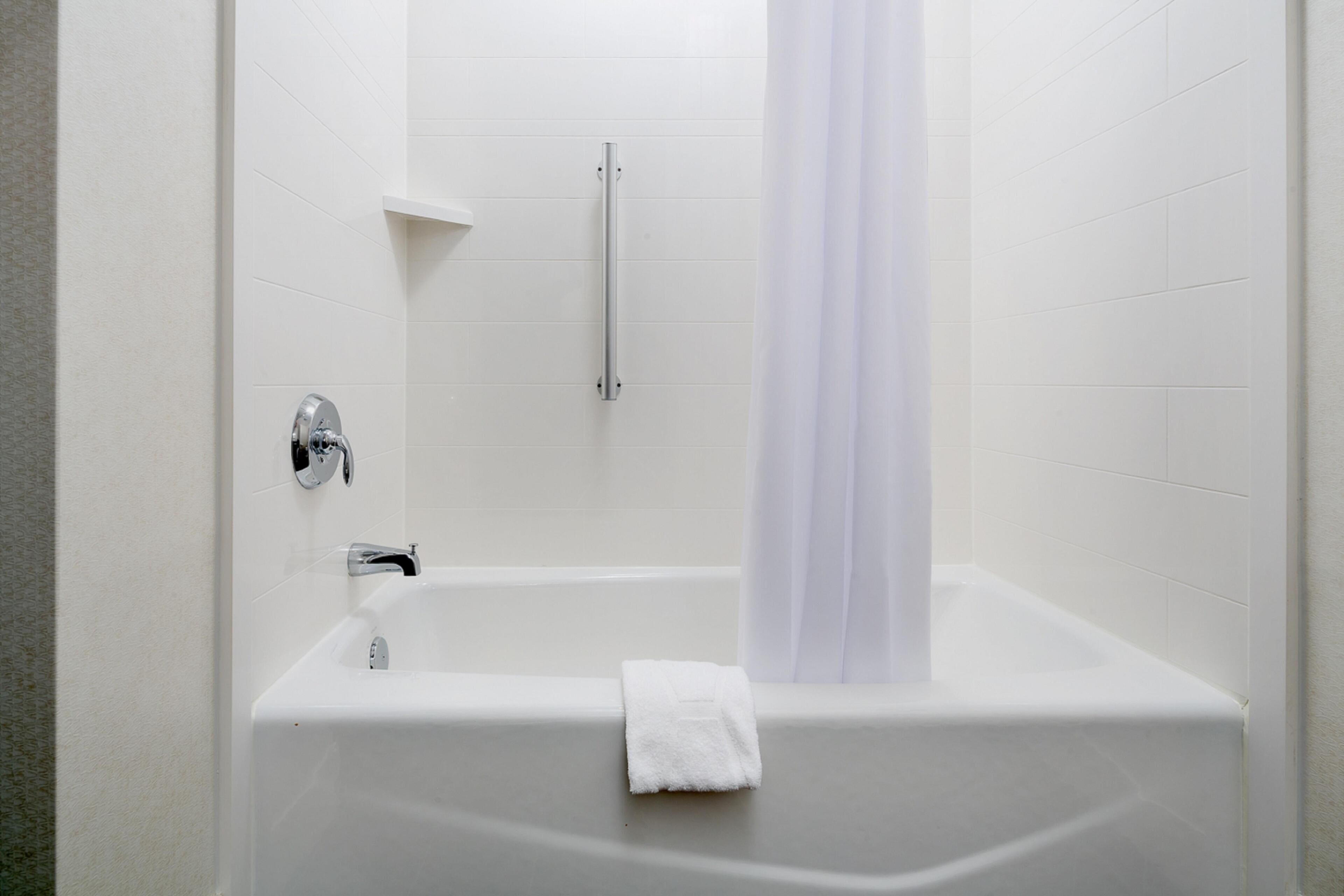 A white bathtub with a towel, a shower curtain, and a grab bar.