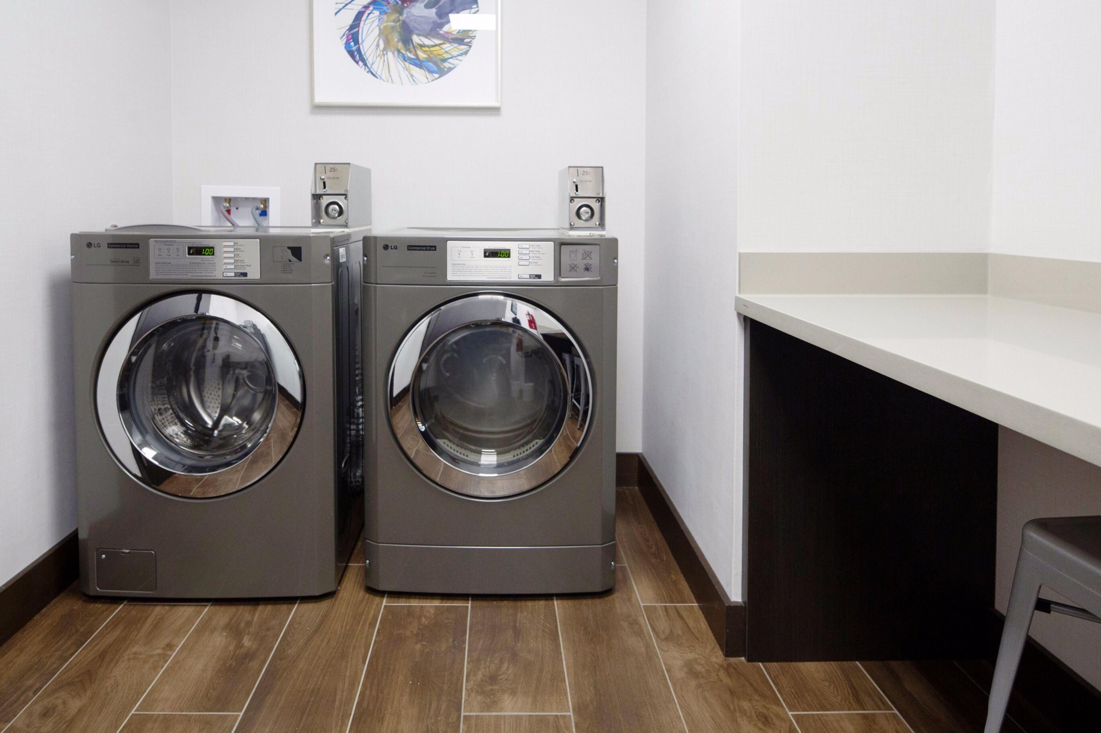 Two front-loading LG washing machines in a laundry room with a white countertop and a framed artwork on the wall.