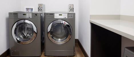 Two front-loading LG washing machines in a laundry room with a white countertop and a framed artwork on the wall.