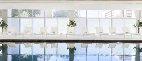 An indoor swimming pool with white lounge chairs and potted plants.